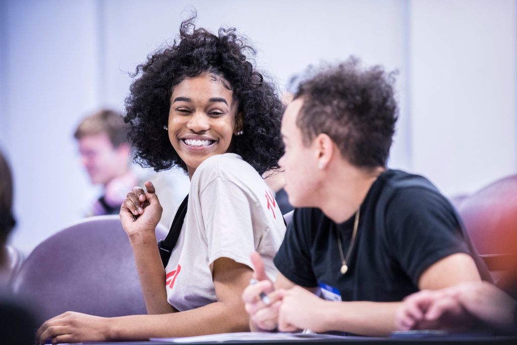 A young black woman with braces and glasses smiles at the camera