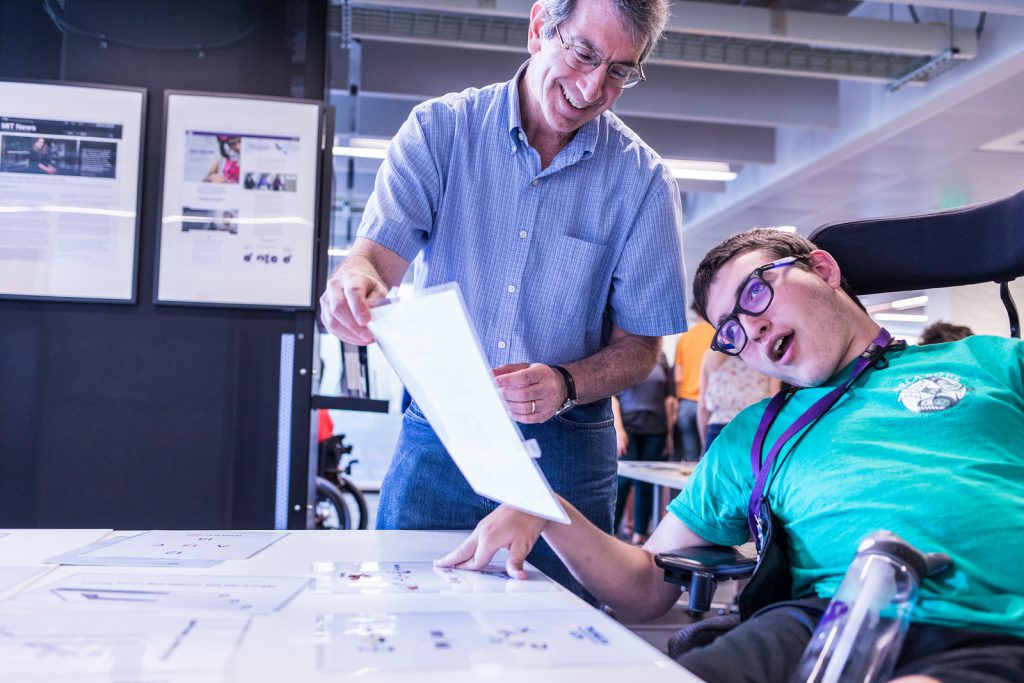 Young male with mobility issues works with an older man to read a paper