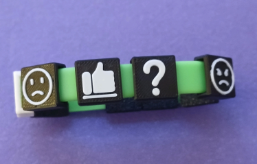 a plastic 3D-printed bracelet with tactile charms with raised icons (frowning face, thumbs up, question mark, angry face)
